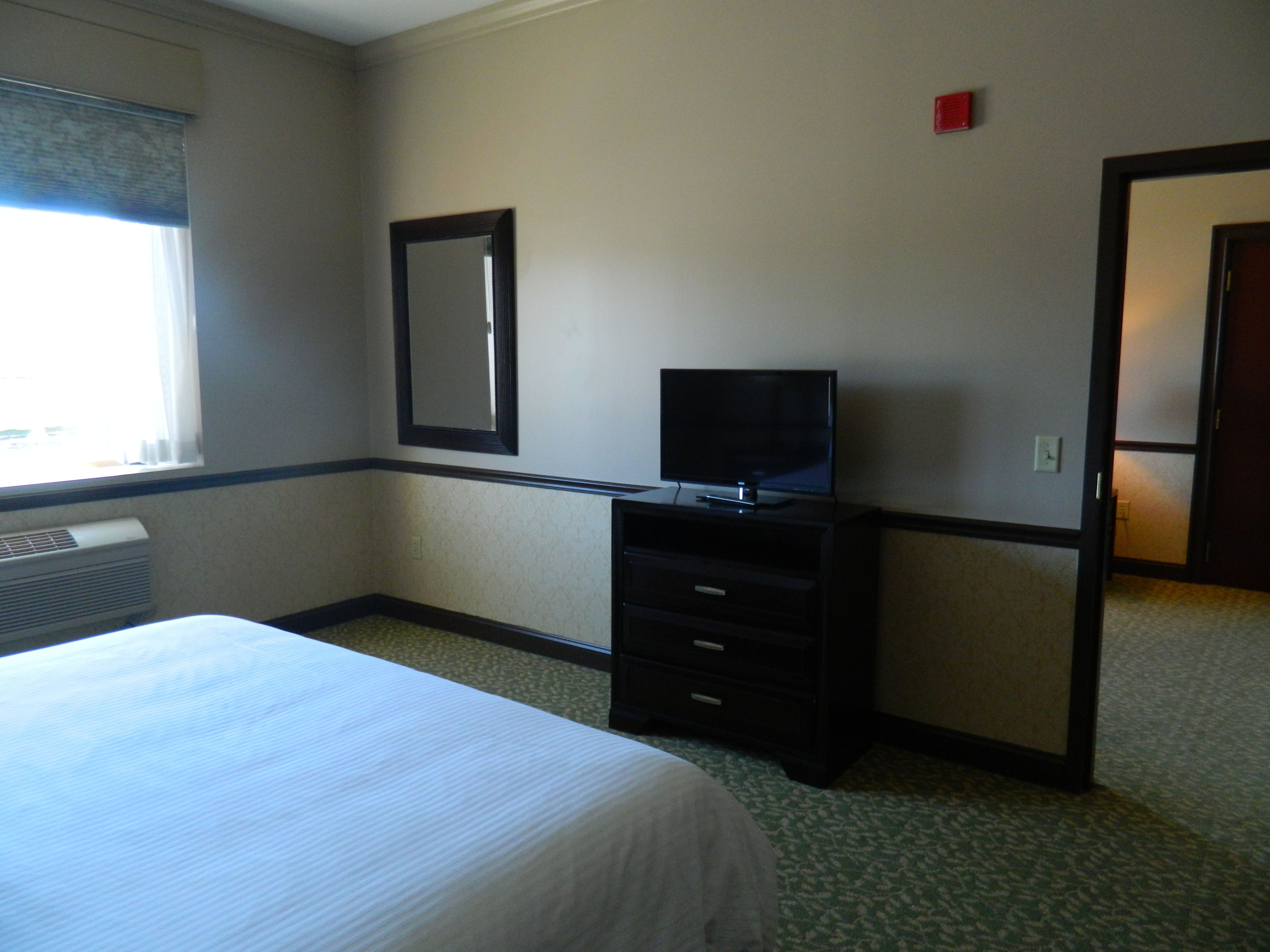 A hotel room with a bed, a television on a dresser, a mirror on the wall, and a window with blinds.