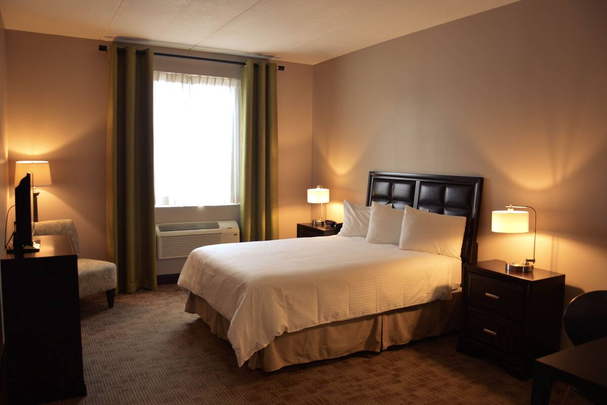 A hotel room with a bed, two bedside tables with lamps, a chair, a desk, and a television.