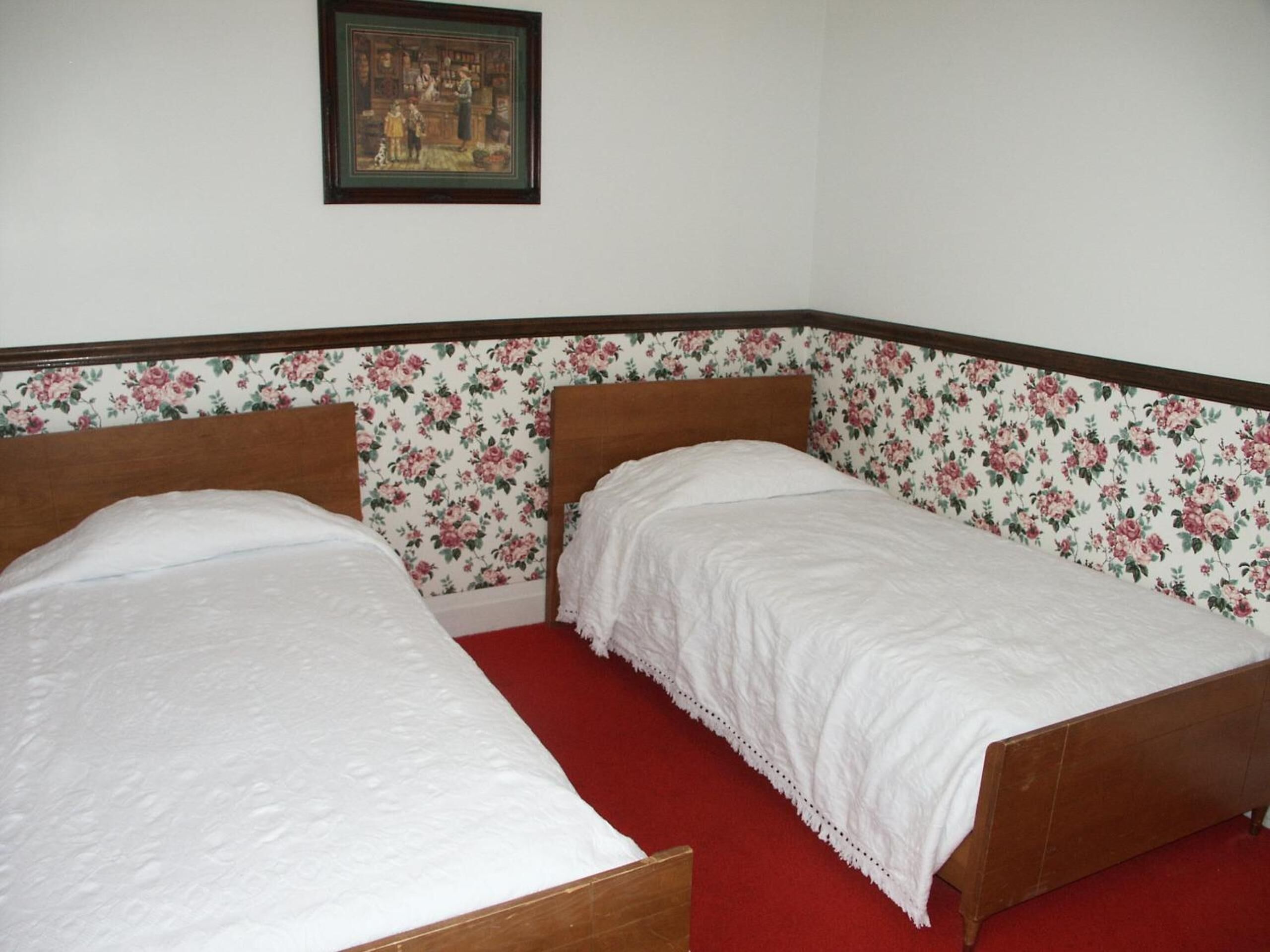 Une chambre avec deux lits simples, un papier peint à motifs floraux et un tableau encadré accroché au mur.