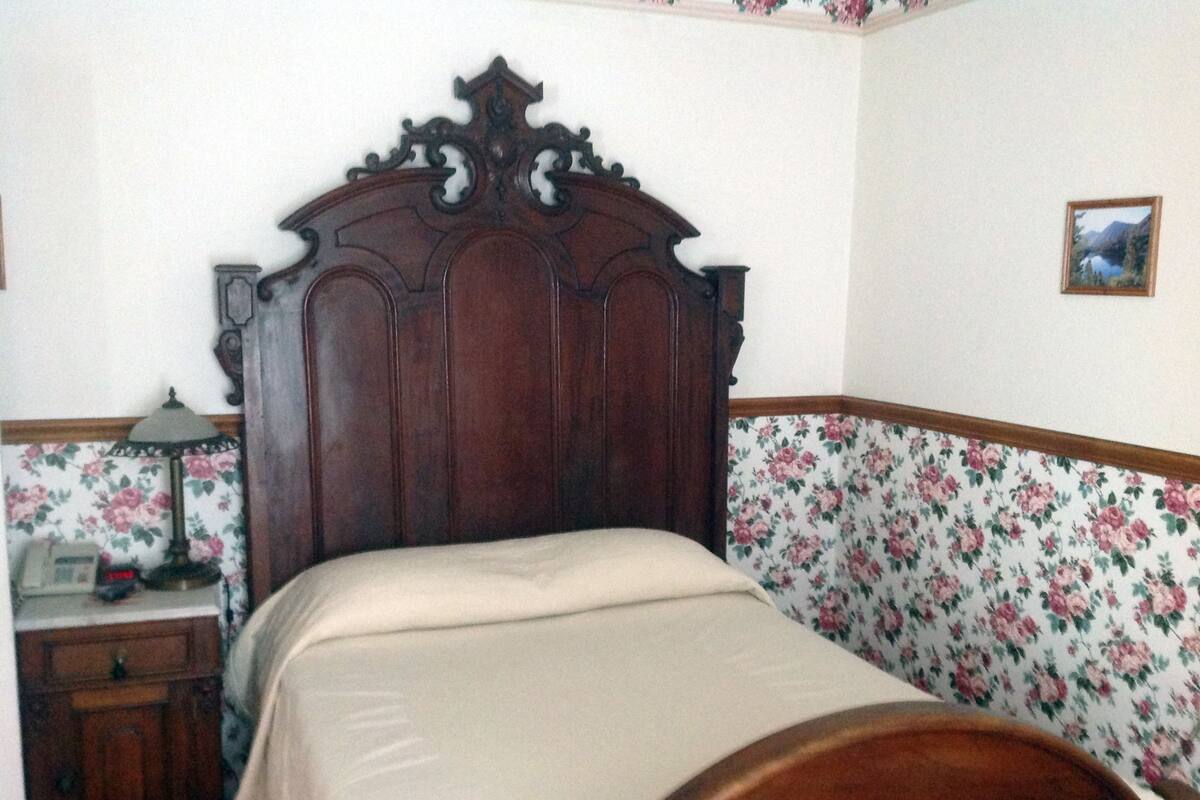 A bedroom with a wooden bed frame, a bedside table with a lamp, and floral wallpaper.