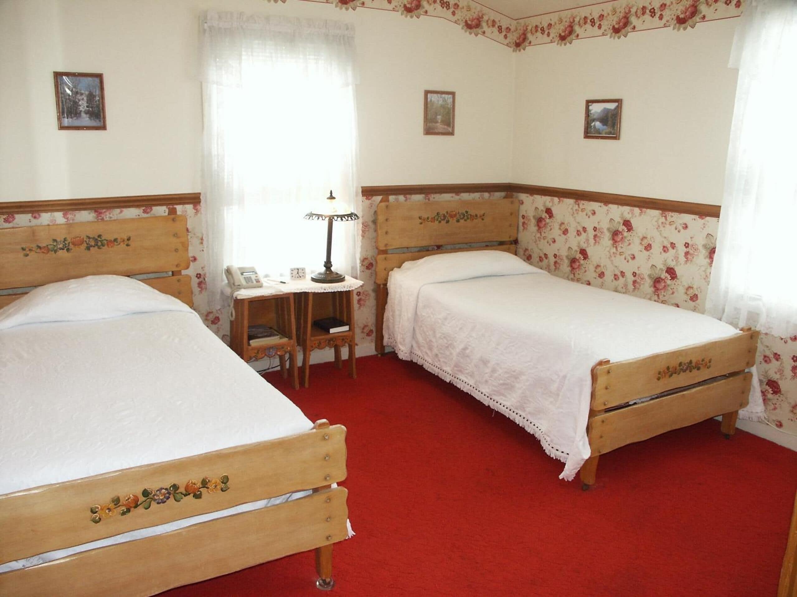 Ein Schlafzimmer mit zwei Holzbetten, einem kleinen Schreibtisch mit Lampe und blumigem Wandpapier.