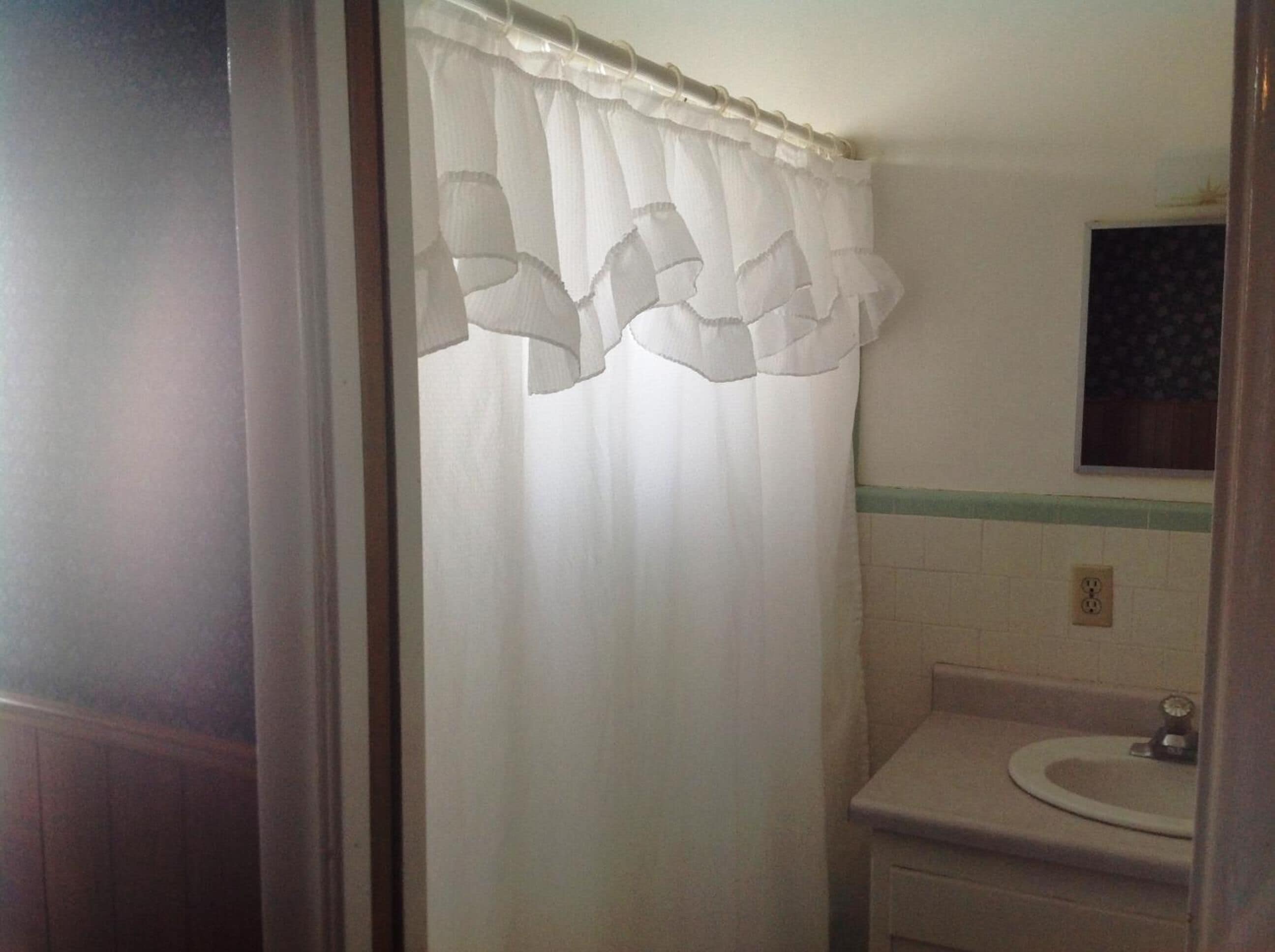 Un baño con cortina de ducha blanca, un lavamanos y un espejo.