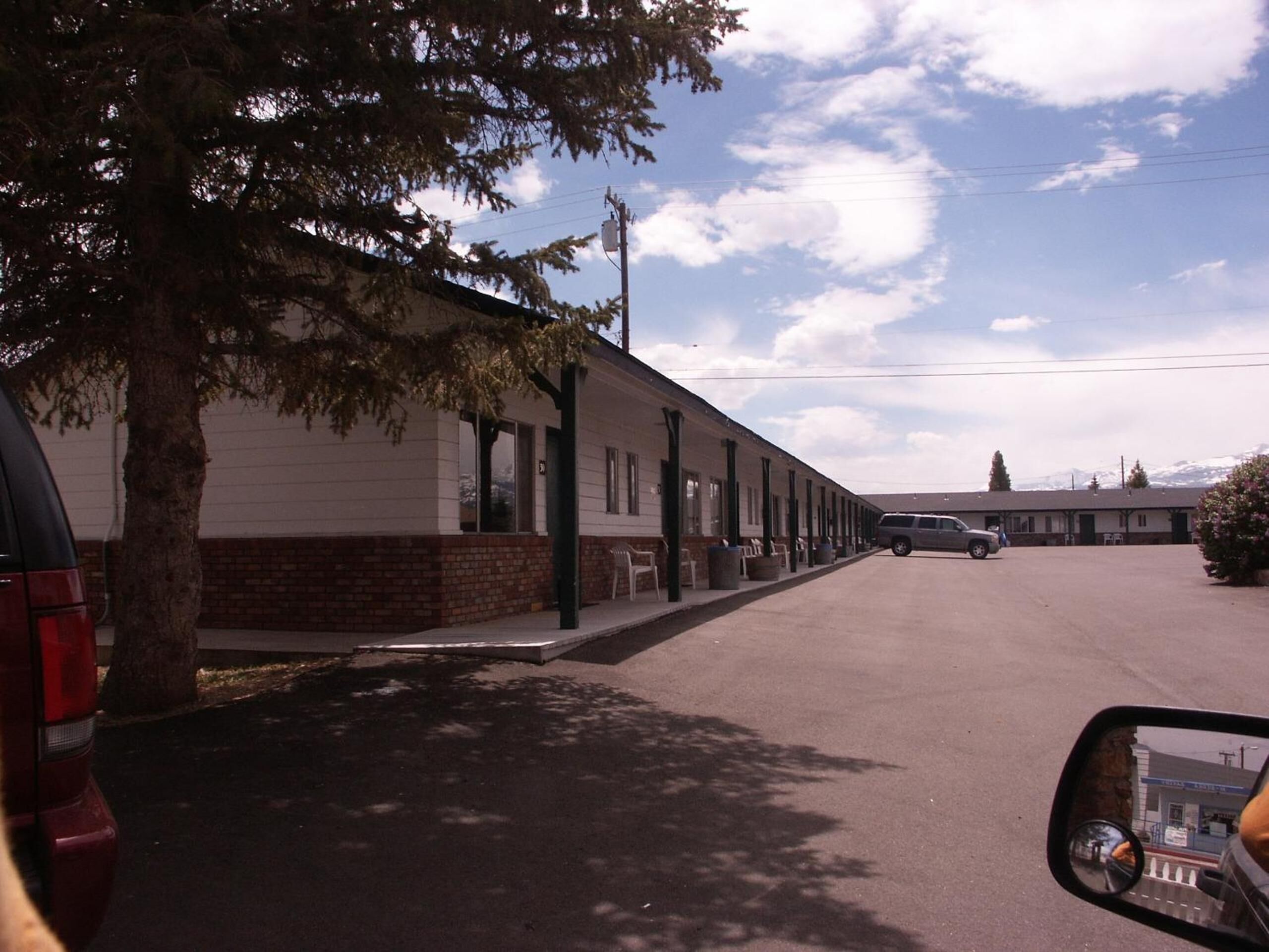 A motel with a row of rooms, a parking lot, and a mountain backdrop.