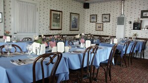 A formal dining room with tables set for multiple guests, featuring floral wallpaper, framed artwork, and American flags. - Bridgeport Inn (Bridgeport)