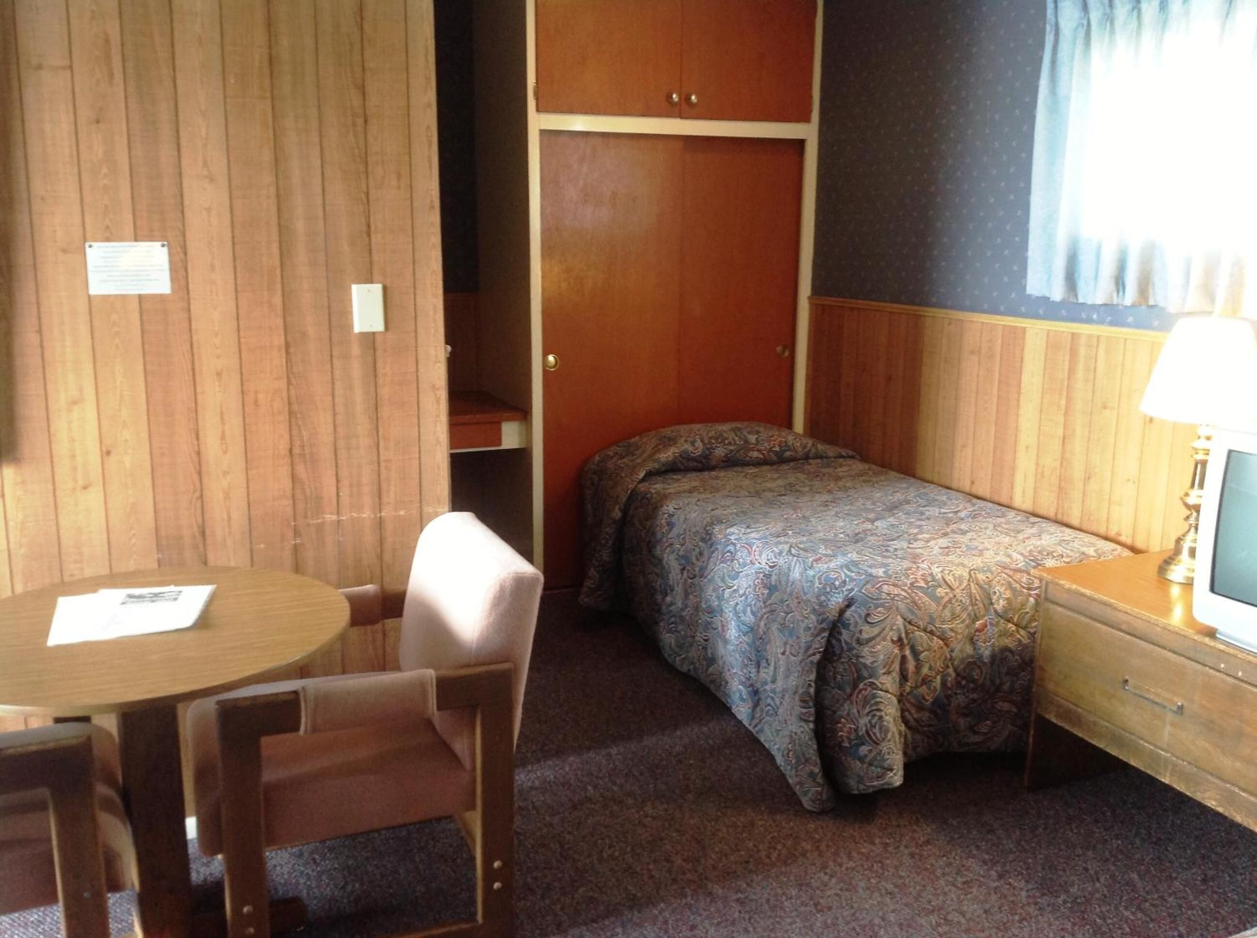 A small room with a bed, a chair, a table, and a TV.