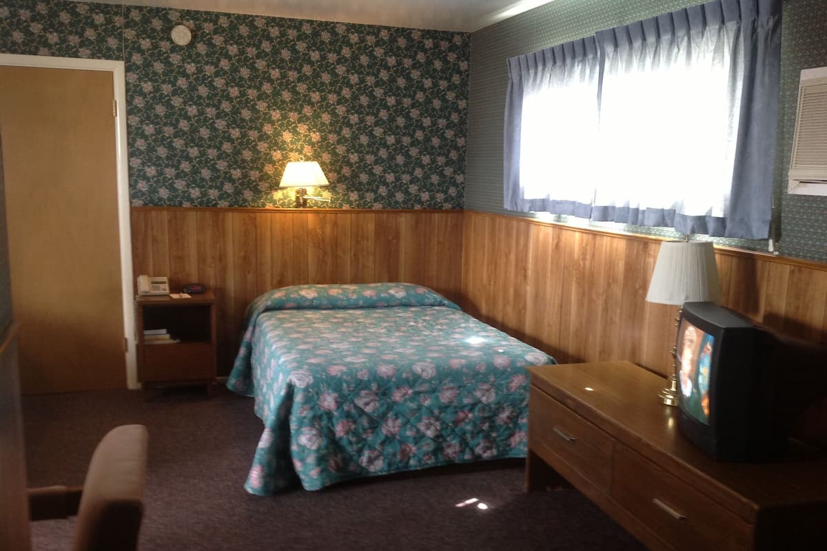 A bedroom with two beds, a wooden dresser, a television, and a lamp.