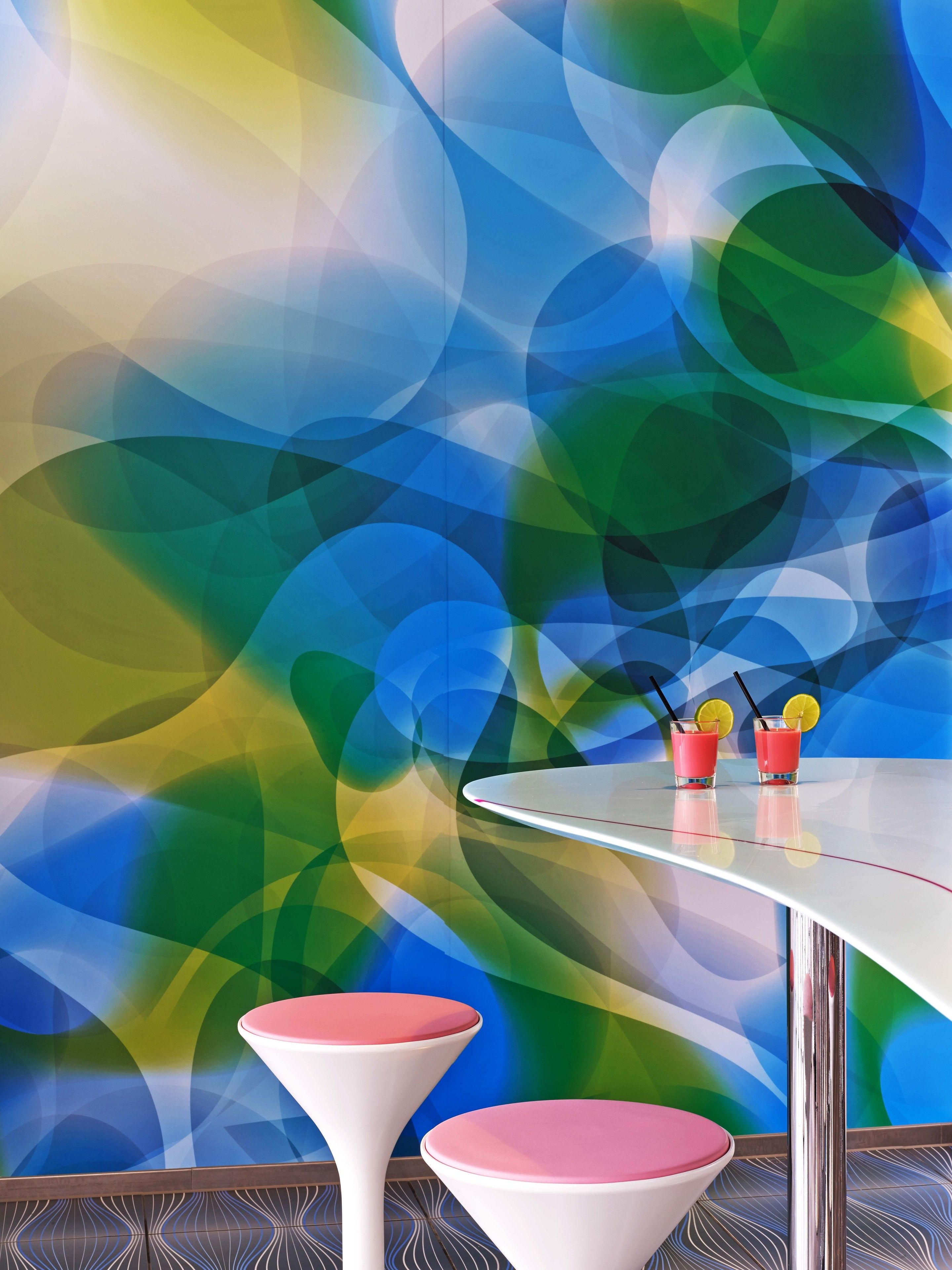 A modern bar area with a colorful abstract wall design, two stools, and two glasses of red drink with lemon slices.