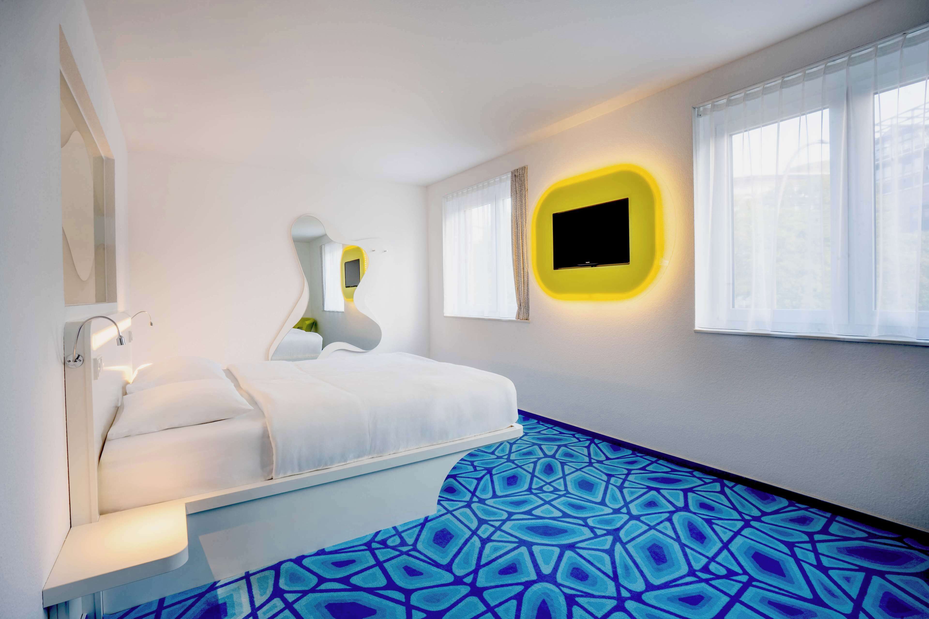 Una habitació d'hotel moderna amb un llit, una taula de nit, un televisor penjat a la paret i un paviment amb dibuixos.