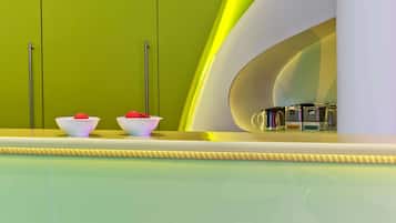 A modern kitchen with green cabinets, a white countertop, and two pink and white stools.