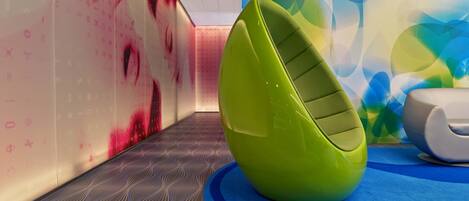 A modern interior with a green pod chair, patterned walls, and abstract wall art.