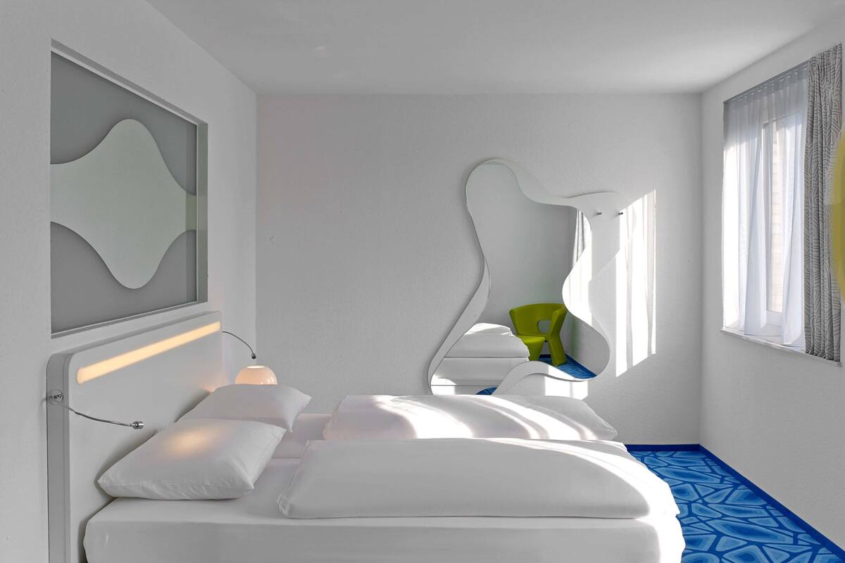 A modern hotel room with a bed, a chair, and a window with curtains.