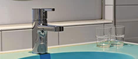 Une salle de bain avec un lavabo moderne, un miroir et deux verres posés sur le comptoir.