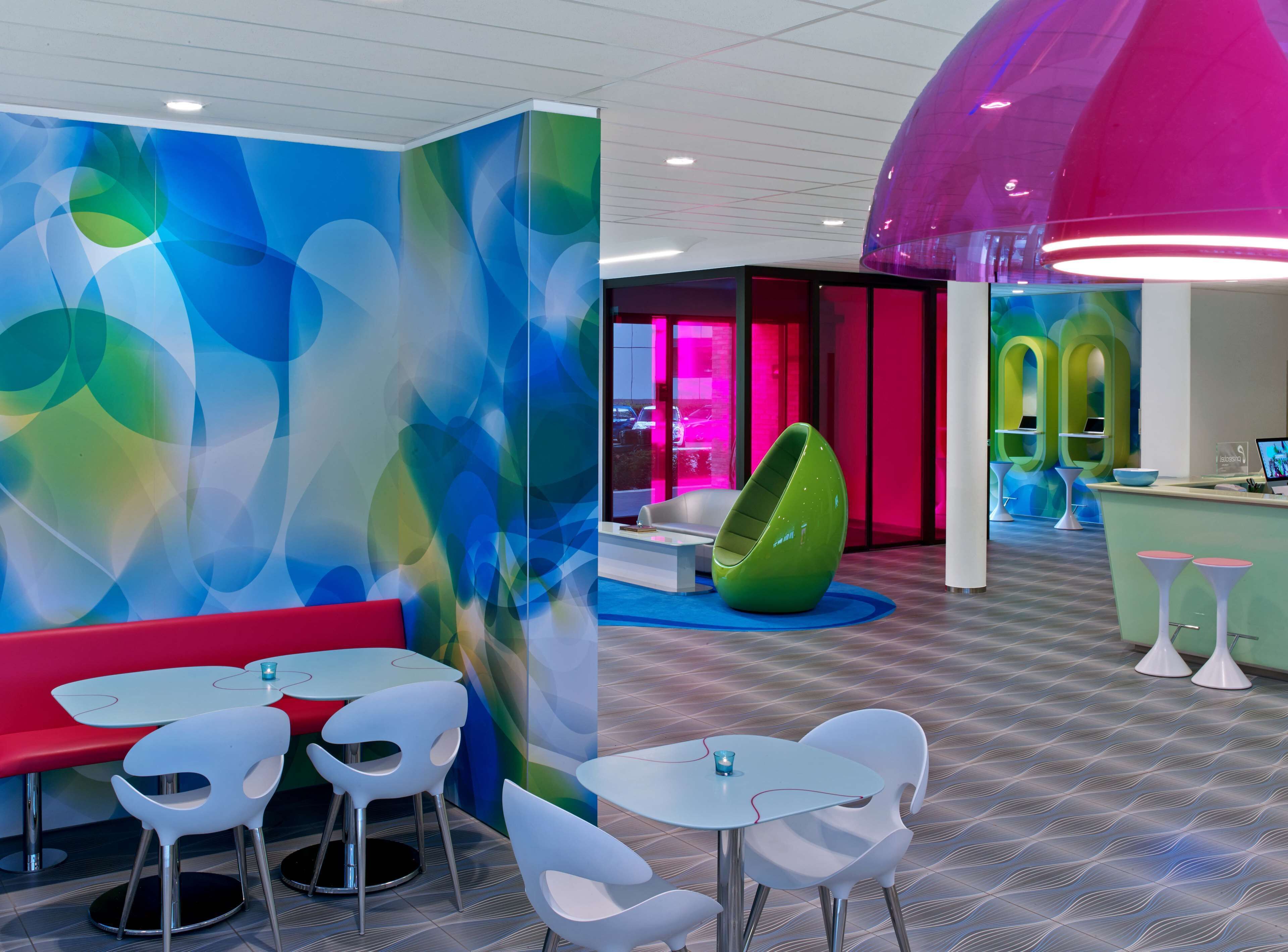 Een modern interieur met kleurrijke abstracte wandkunst, een levendige hanglamp en een groene, eivormige fauteuil.