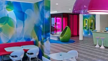 Ein modernes Interieur mit farbenfroher abstrakter Wandkunst, einer leuchtenden Hängelampe und einem grünen, ei-förmigen Sessel.