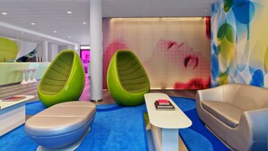 Een moderne lobby met groen en beige zitplaatsen, een receptiebalie en een kleurrijke muurschildering.