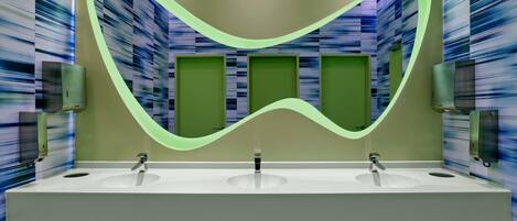 A modern bathroom with two sinks, green accent walls, and a neon light design.
