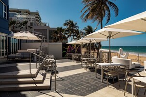 Un bar en la azotea con mesas al aire libre, palmeras y vistas a la playa.