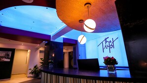 A reception area with a modern design, featuring a reception desk, a large illuminated sign, and potted plants.