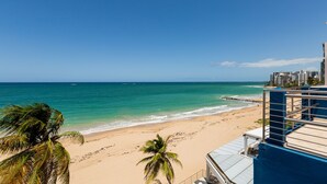 A beach view with clear skies, palm trees, and a building with a blue roof.