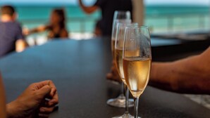 Two glasses of champagne on a table with a view of the ocean and people in the background.
