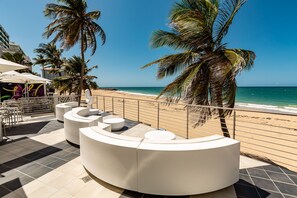 A beachside lounge with white seating and a view of the ocean. - The Tryst Beachfront Hotel (San Juan)