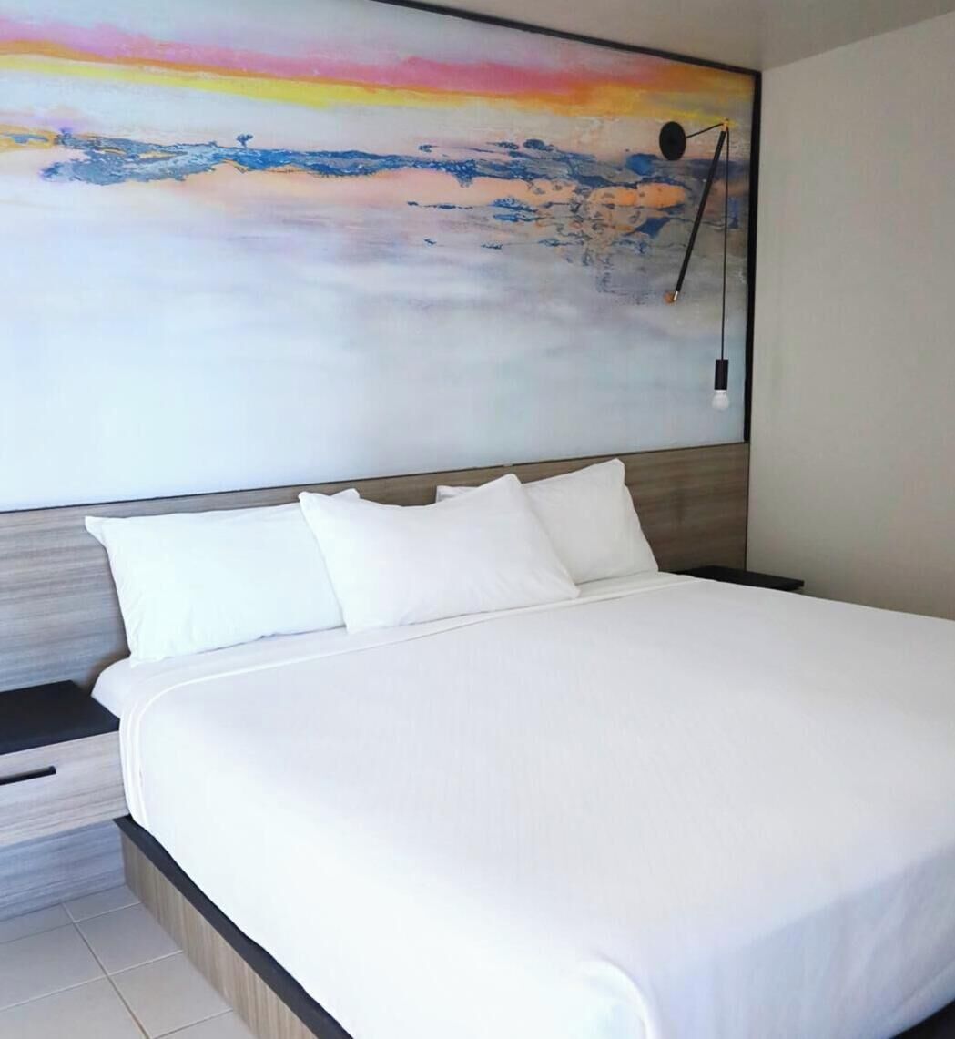 A modern hotel room with a large bed, a nightstand, and a wall-mounted lamp.