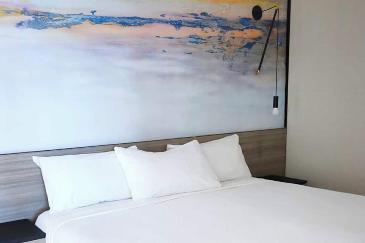 Una habitación de hotel moderna con una cama grande, una mesita de noche y una lámpara de pared.