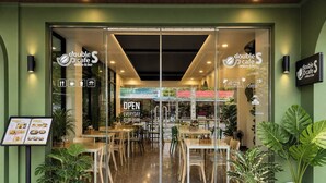 Un caffè con ingresso in vetro, posti a sedere interni e un tappeto di benvenuto.