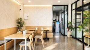 Un interno moderno con tavoli e sedie in legno, una pianta in vaso e una porta vetrata che dà sull'esterno.