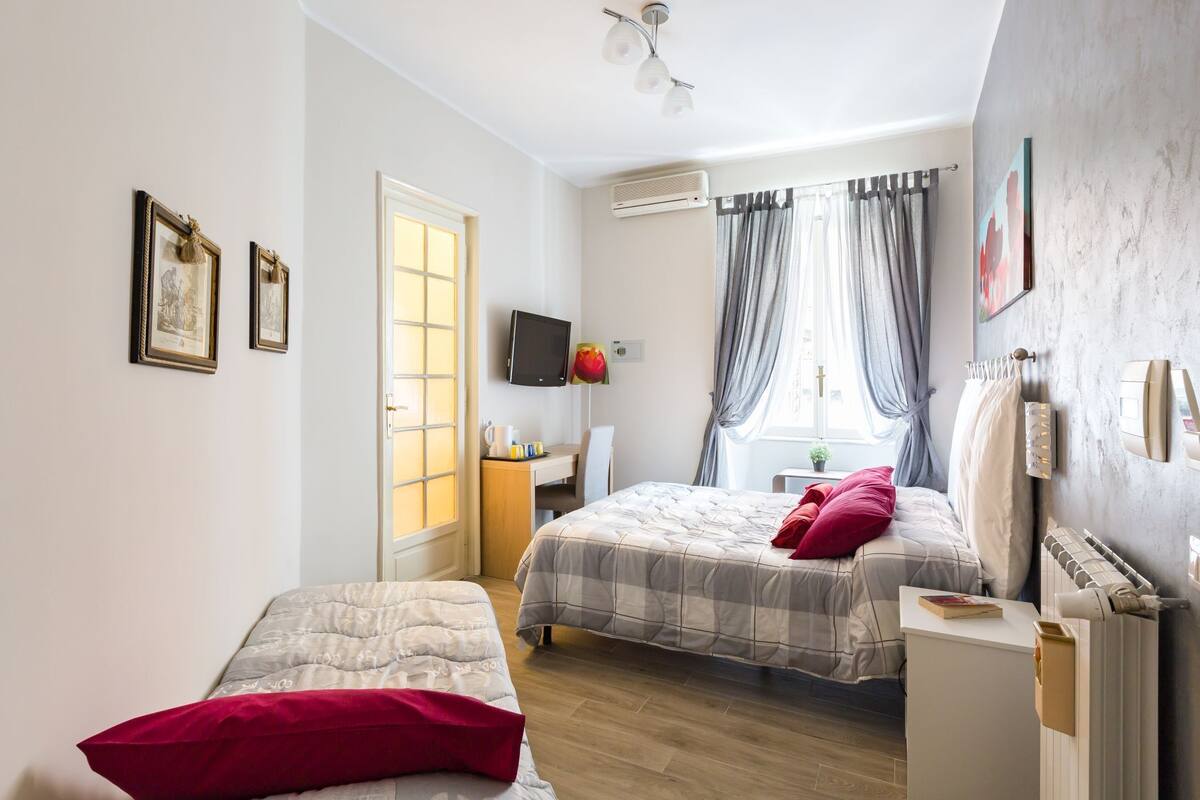 A bedroom with two beds, a desk, a TV, and a radiator.