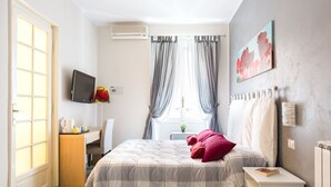 A bedroom with a bed, a desk, a chair, a TV, and a window with curtains. - Guest House Calamatta (Rome)