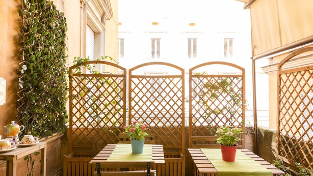 An outdoor seating area with wooden tables and chairs, potted plants, and a lattice partition. - Guest House Calamatta (Rome)