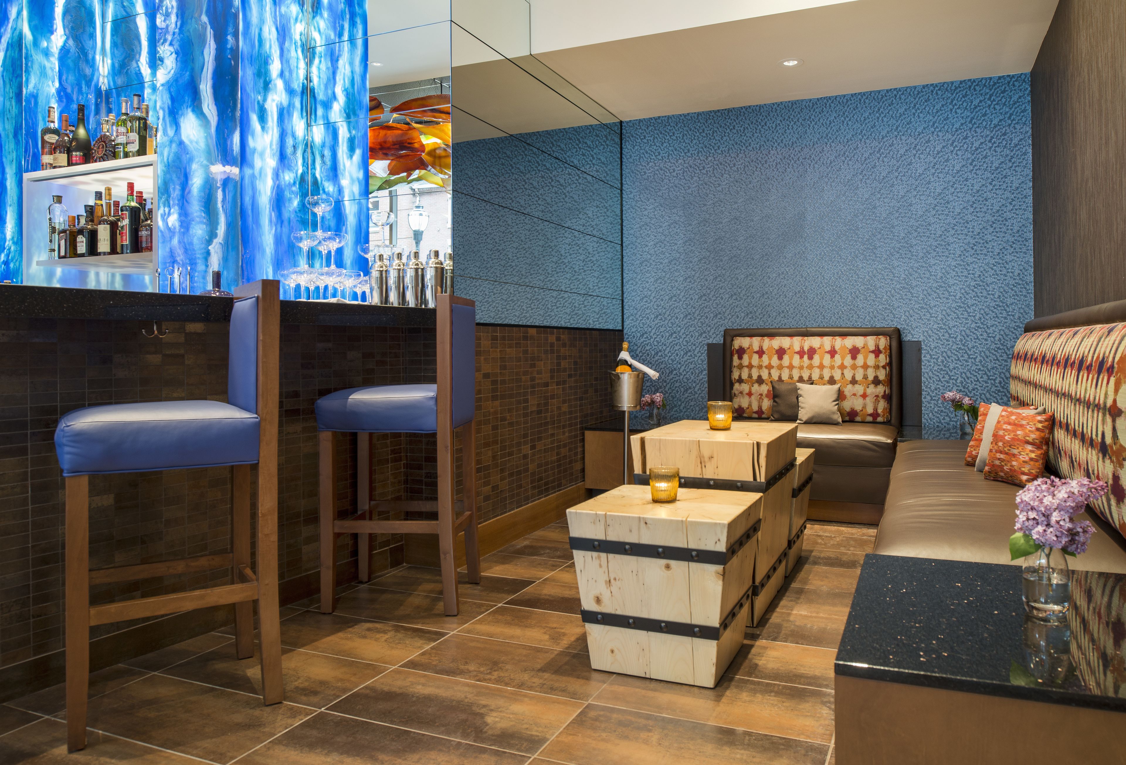 A bar area with stools, a counter with bottles, and a seating area with a sofa and cushions.