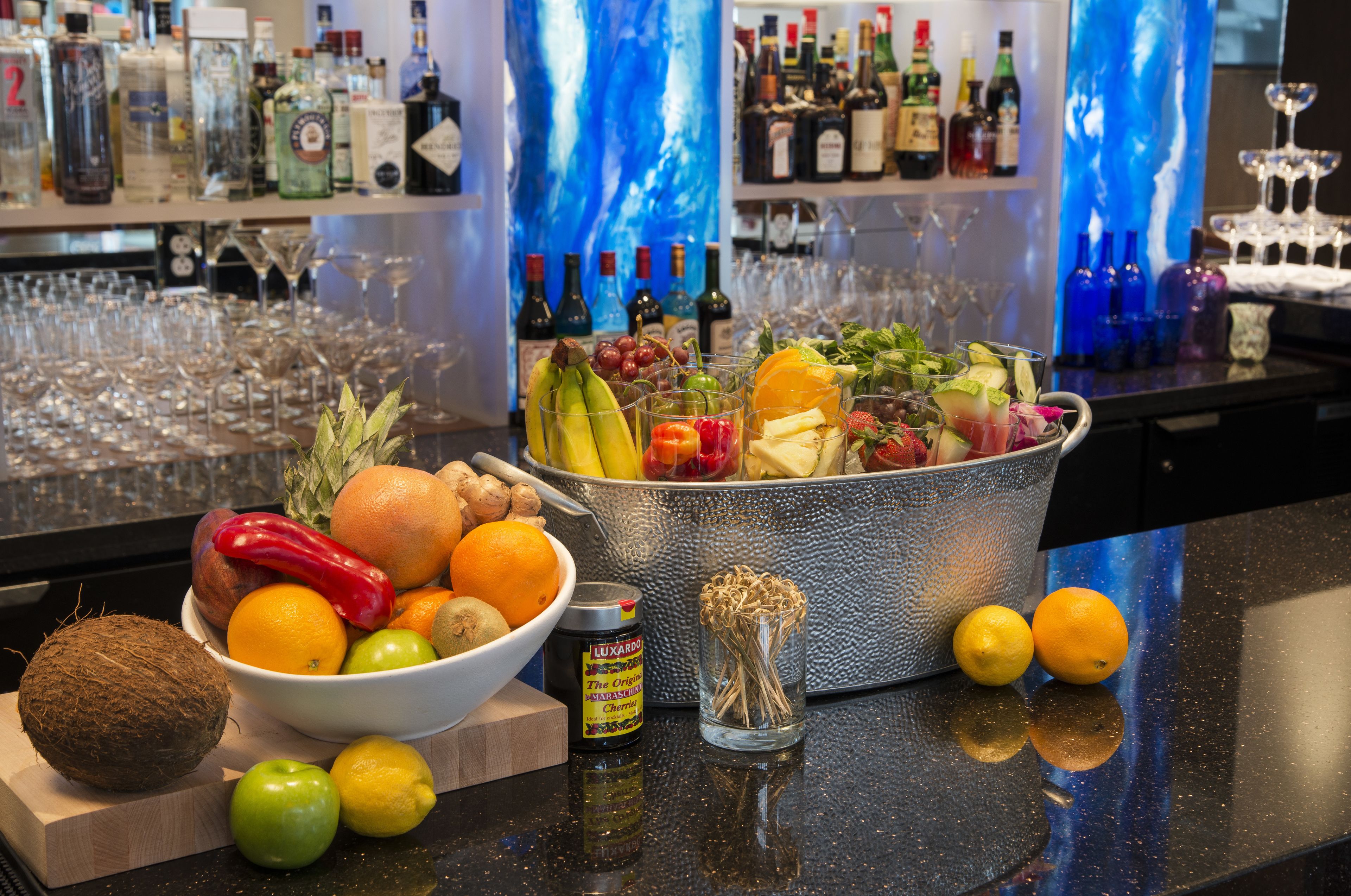 A bar area with a variety of fruits, bottles, and glasses.