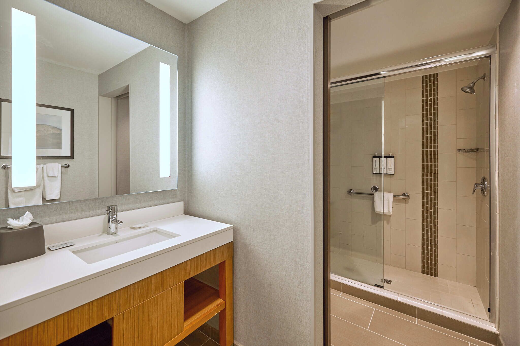 Un baño moderno con un espejo grande, dos lavabos, ducha y tocador de madera.