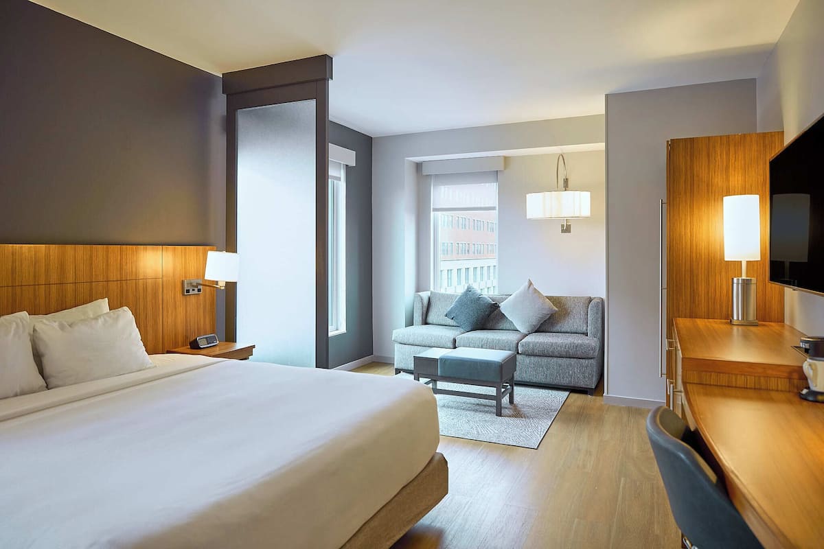 A hotel room with a large bed, a sofa, a desk, and a TV.