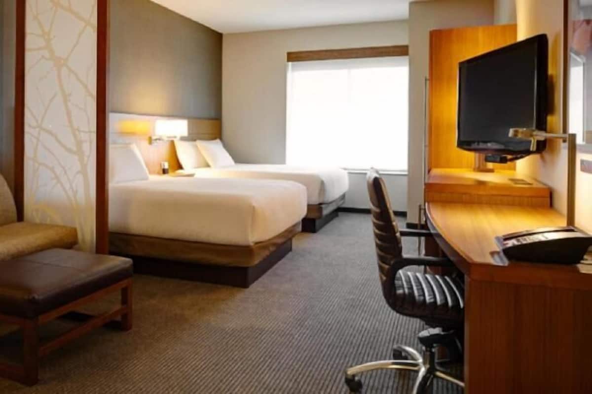 A hotel room with a sofa, two beds, a desk with a chair, and a TV.