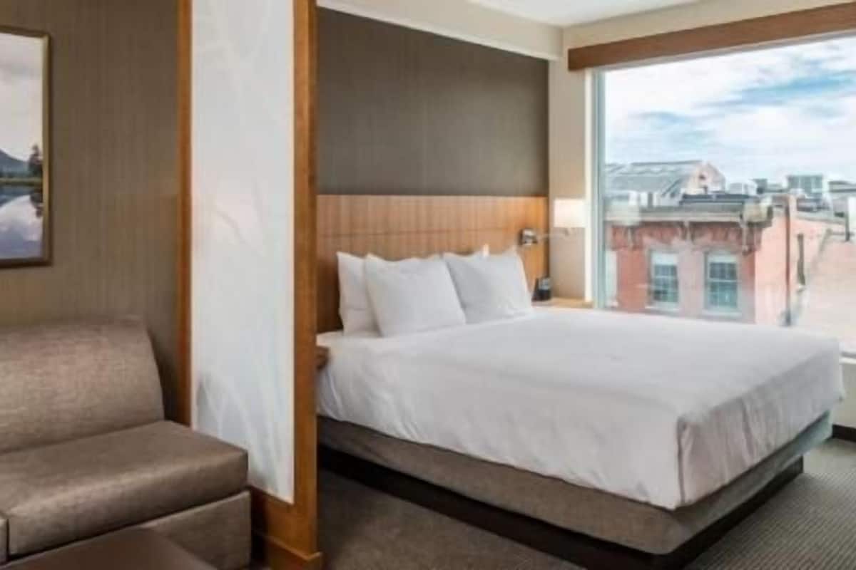 A hotel room with a bed, a sofa, a large window, and a painting on the wall.