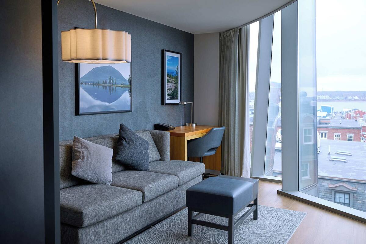 A modern living room with a sofa, a desk, and a large window with a city view.