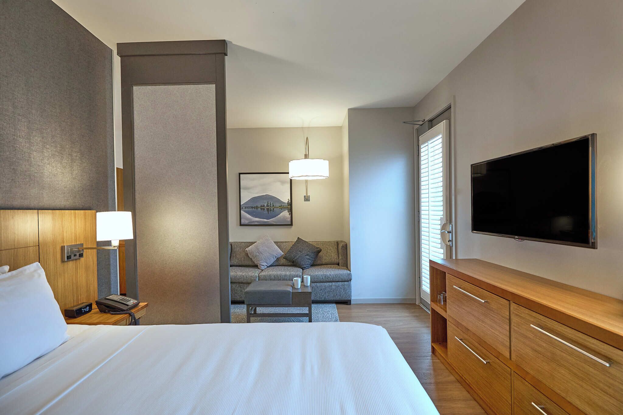 Une chambre d’hôtel comprenant un lit, une table de chevet, une lampe, une télévision, un canapé et une commode en bois.