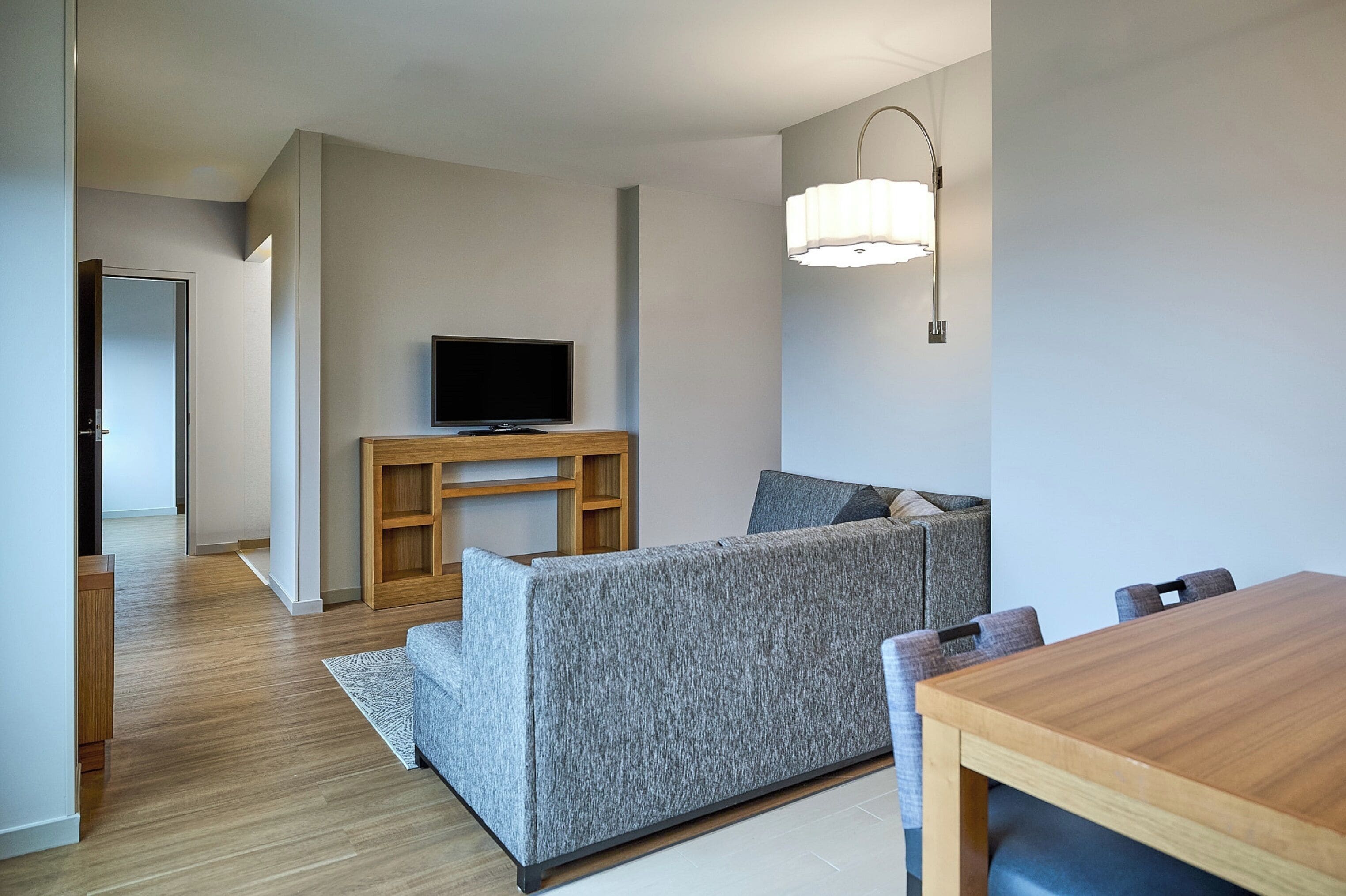 Una sala de estar moderna con un sofá gris, una mesa de centro de madera, un televisor de pantalla plana y una mesa de comedor con sillas.