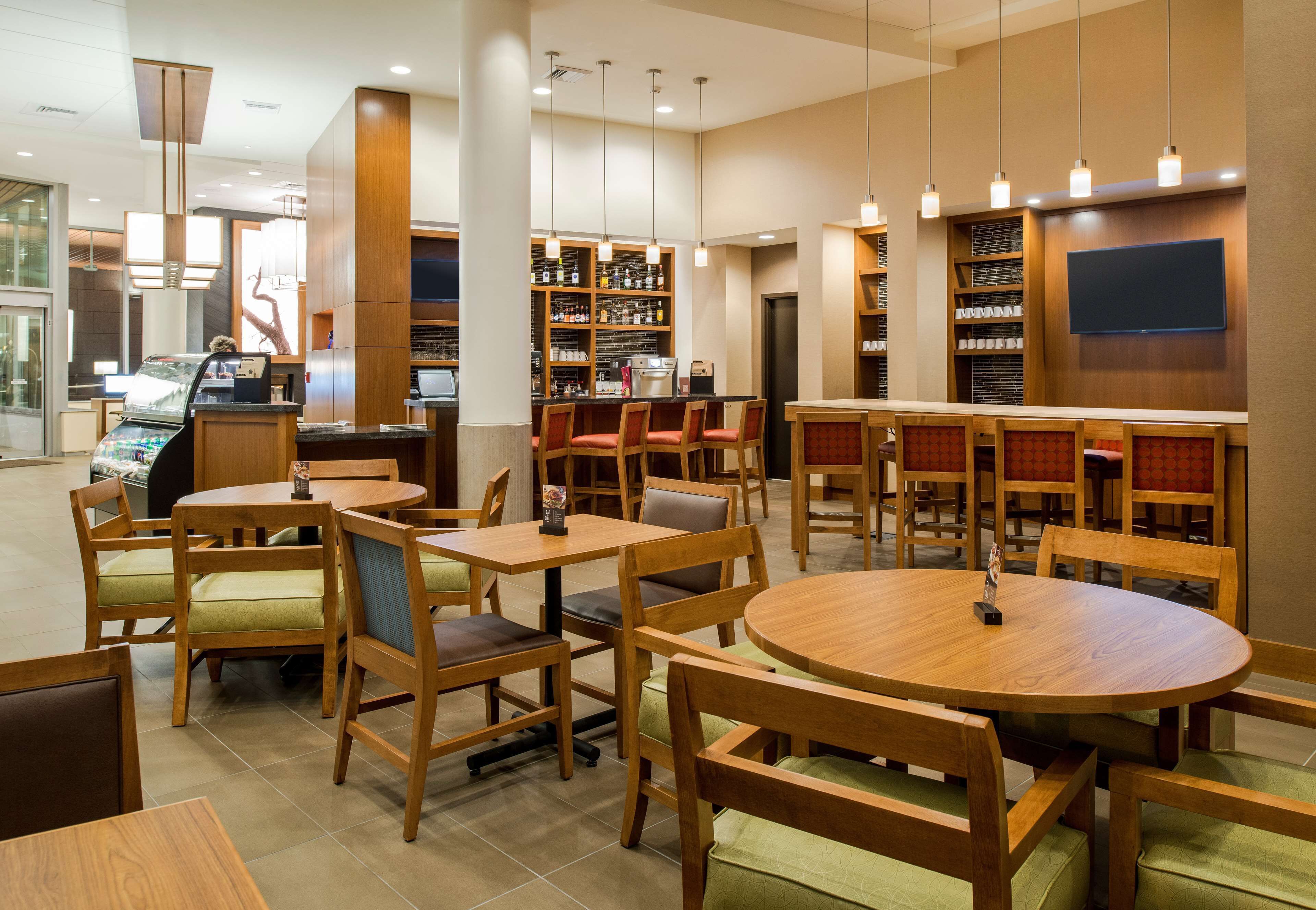 A modern restaurant with wooden furniture, a bar area, and a large screen on the wall.