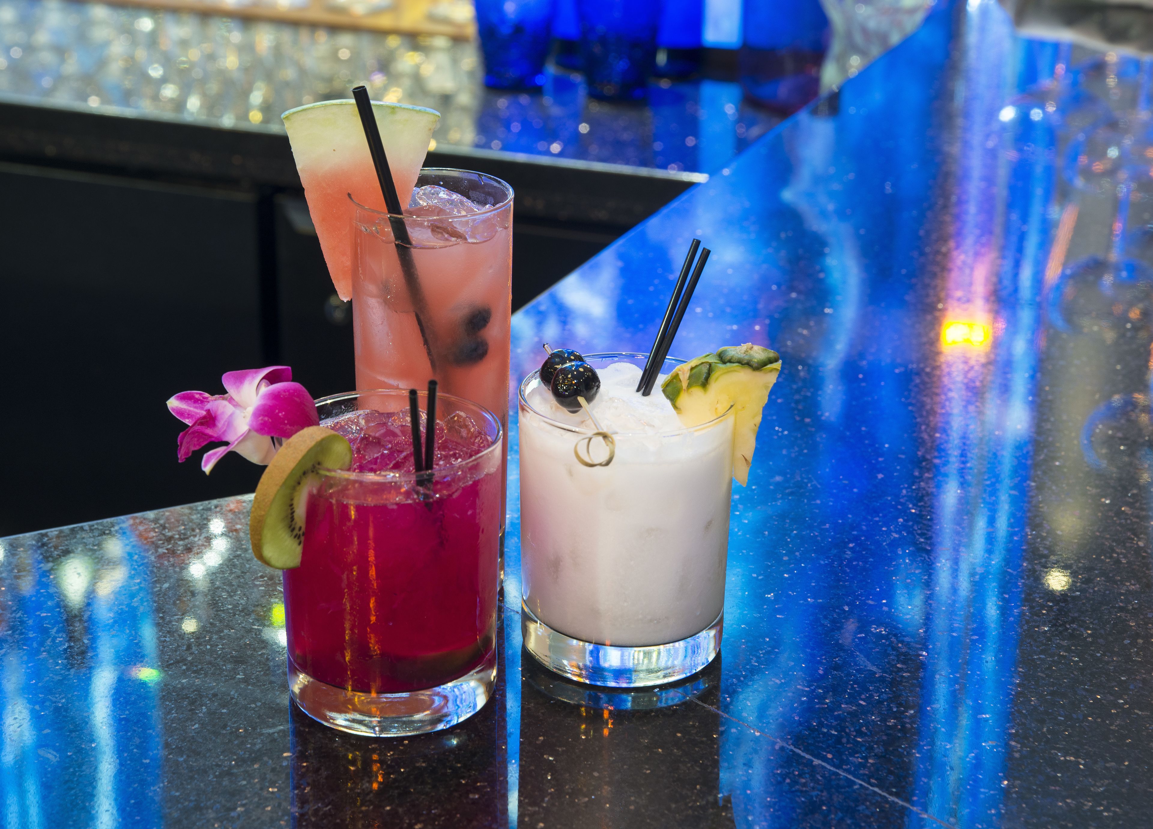 Trois cocktails sont posés sur le comptoir d’un bar, dont la surface est réfléchissante.