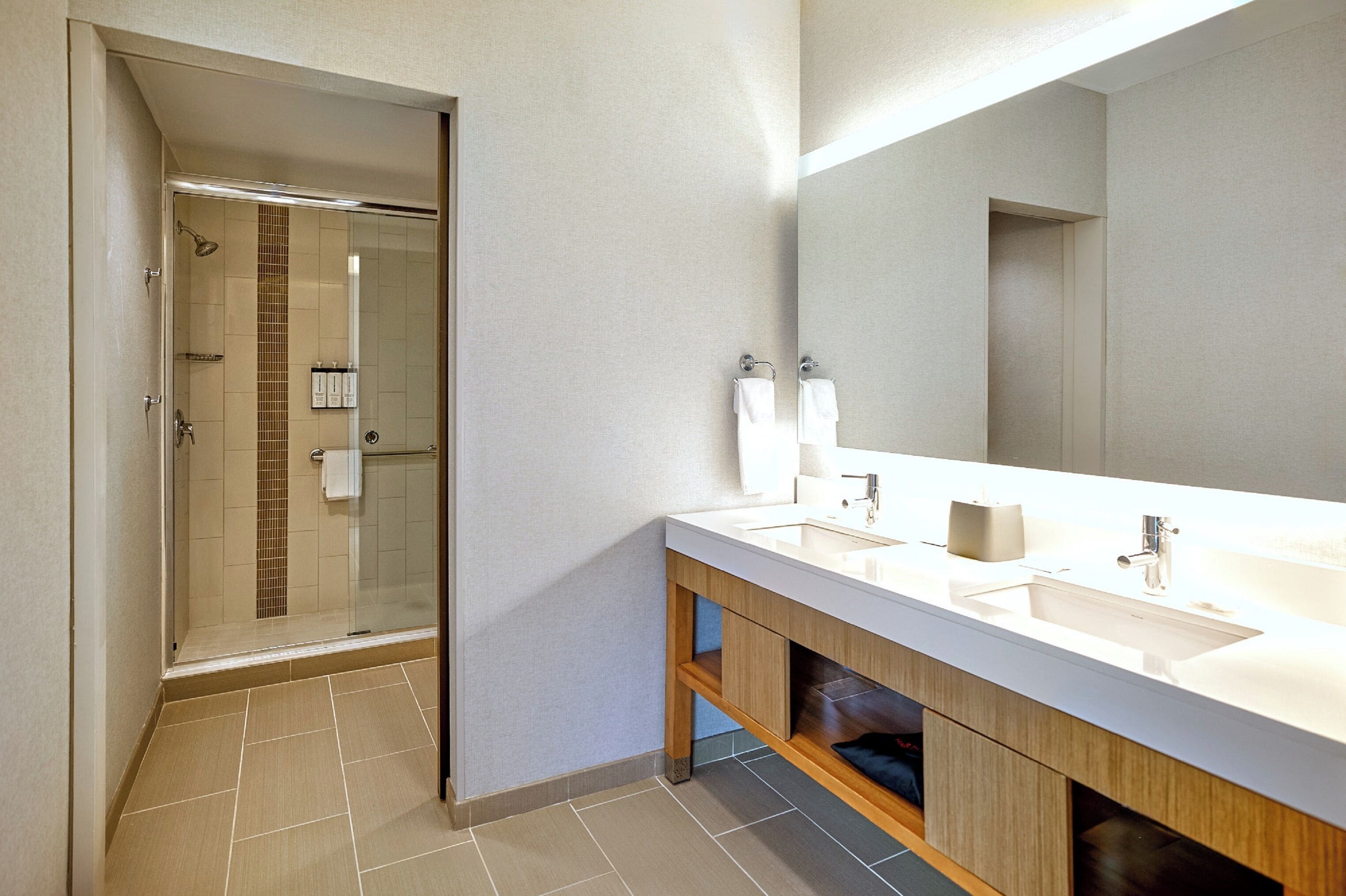 A modern bathroom with a glass-enclosed shower, a large mirror, and a dual sink vanity.