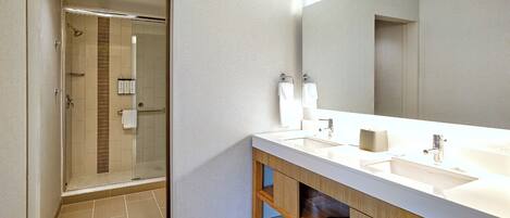 Un baño moderno con ducha envuelta en vidrio, un espejo grande y un mueble de tocador doble.