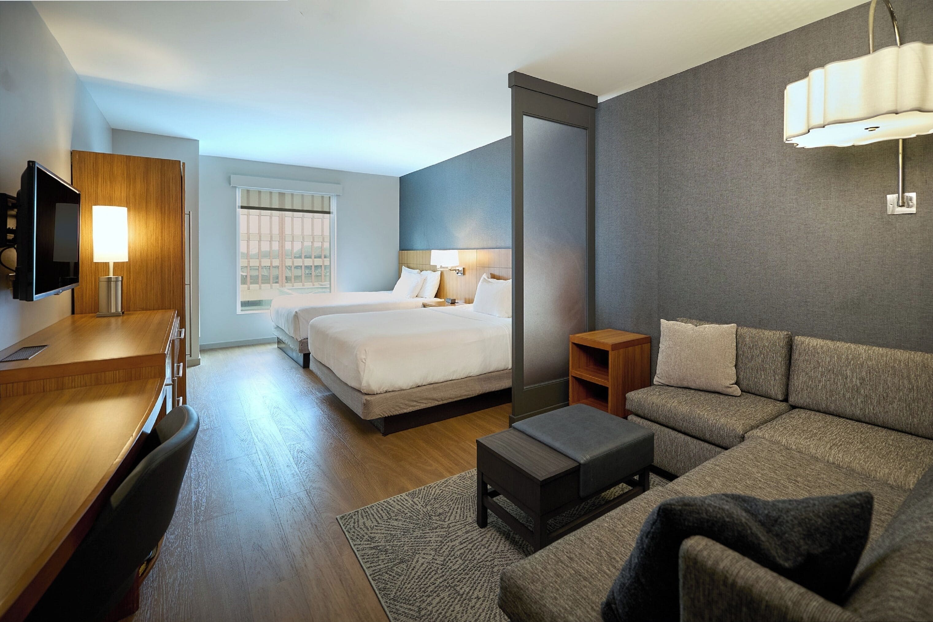 Une chambre d’hôtel avec un bureau en bois, un lit, un canapé et une télévision.