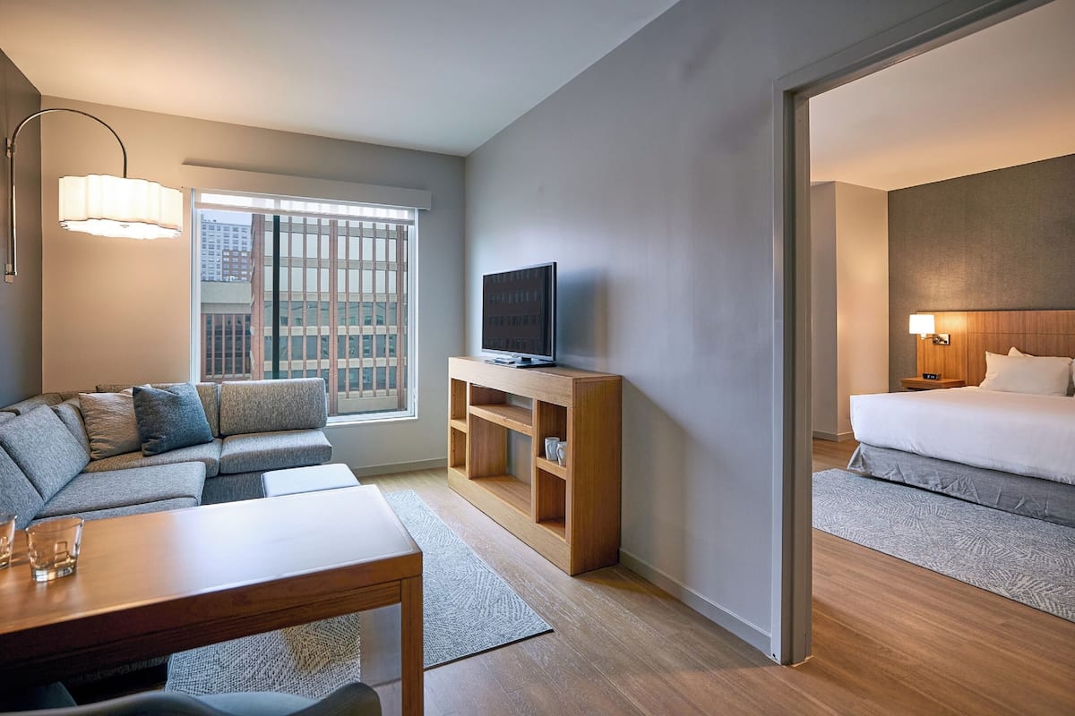 A modern hotel room with a sofa, a TV on a wooden stand, a bed, and a dining area.