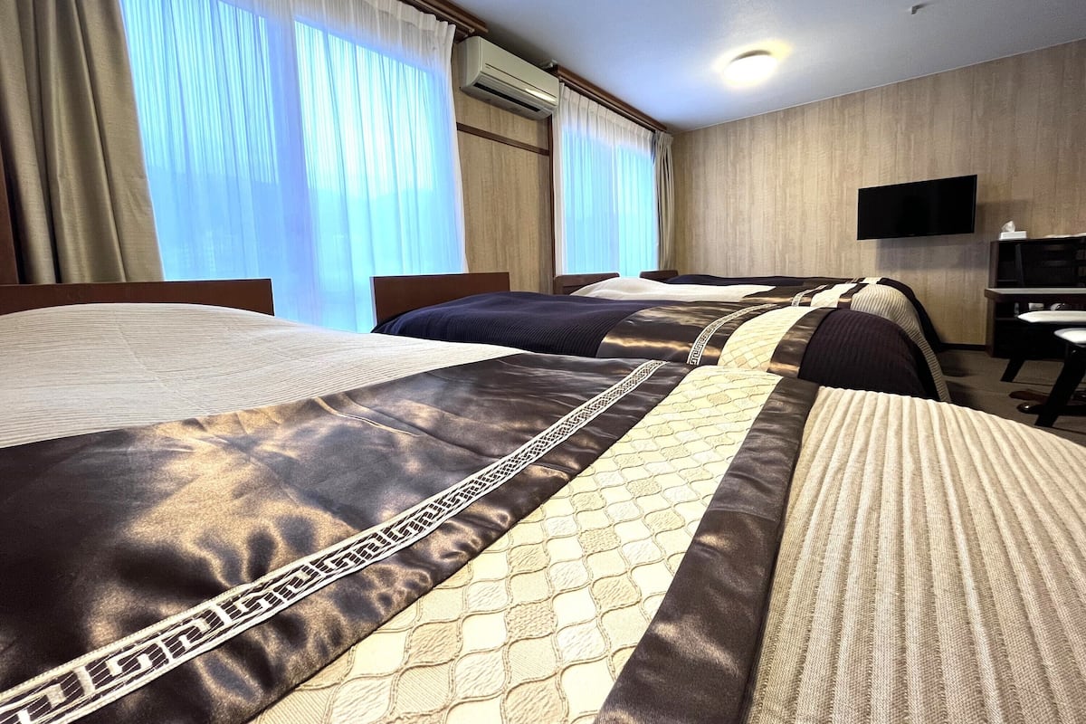 A hotel room with three beds, a flat-screen TV, and a desk.