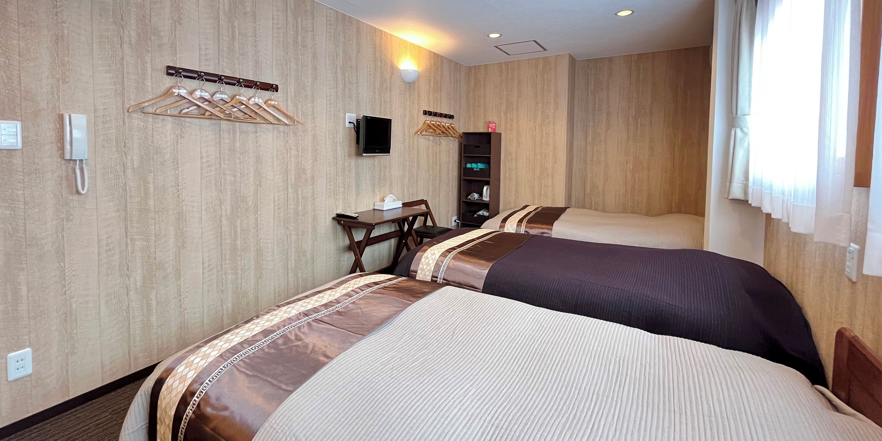 A hotel room with two beds, a desk, a TV, a phone, and a coat rack.