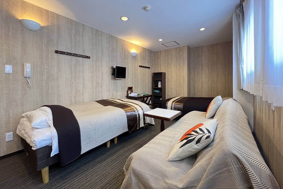 A hotel room with two single beds, a sofa, a desk, a television, and a wardrobe.